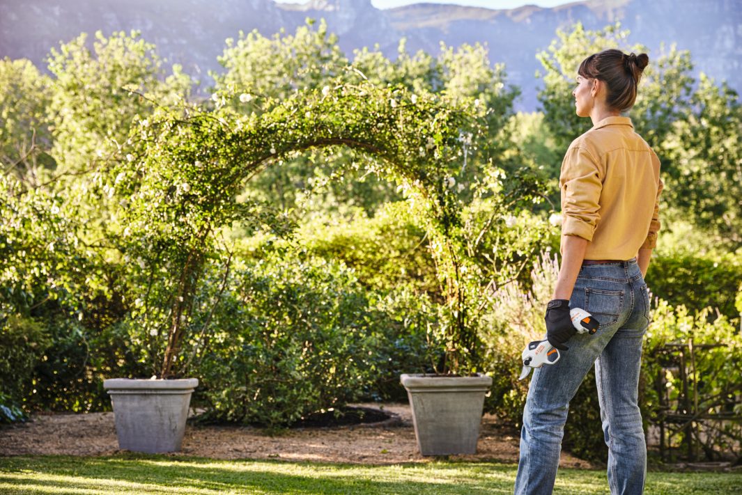 mujer apreciando su jardin con unas tijeras STIHL a bateria en su mano