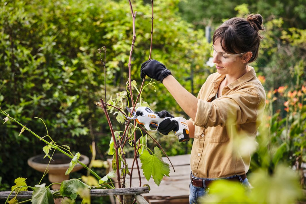 mujer manteniendo su jardin con unas tijeras STIHL a bateria en su mano